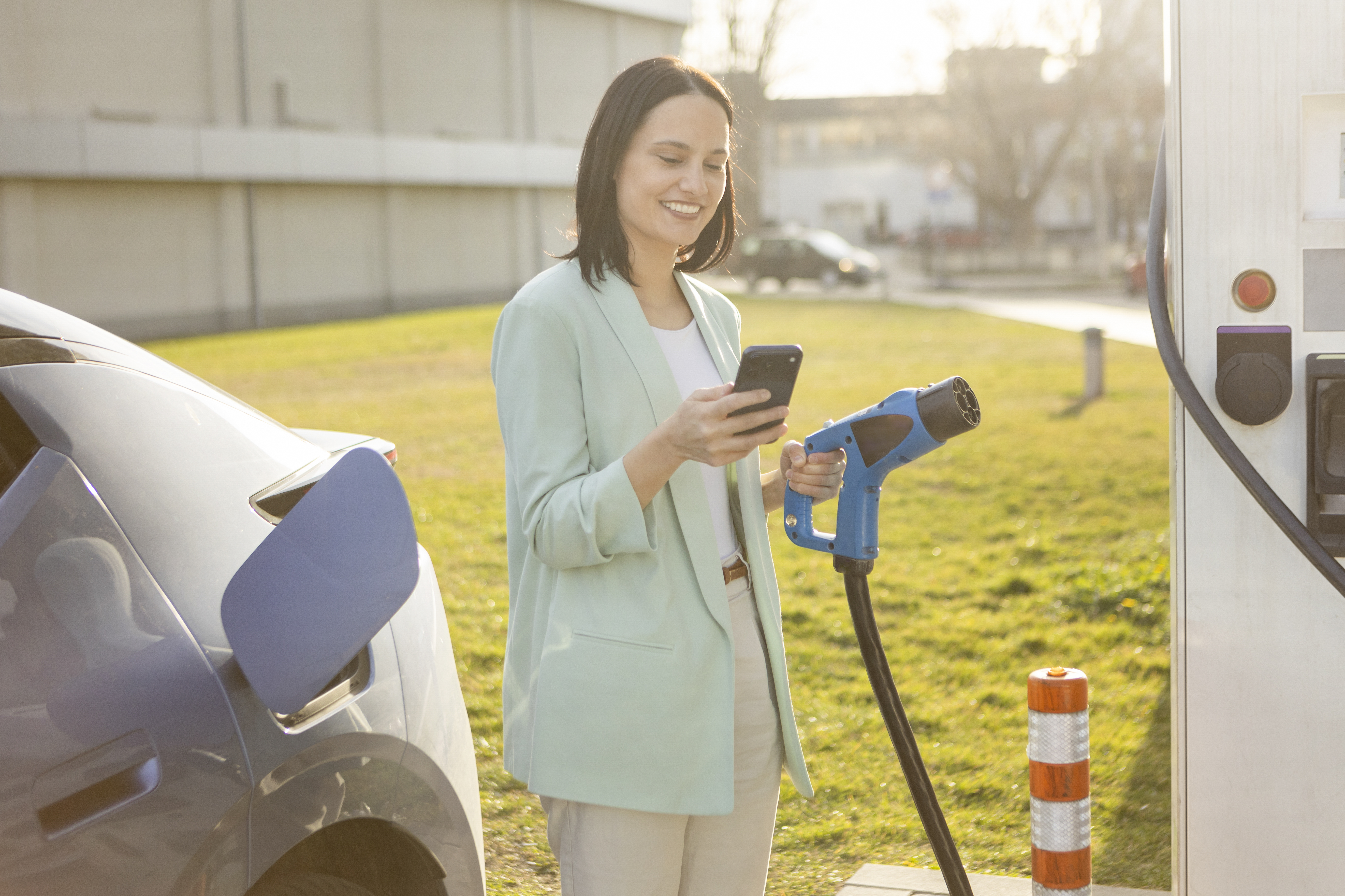 Frau lädt Elektroauto an Ladestation mit Smartphone-App