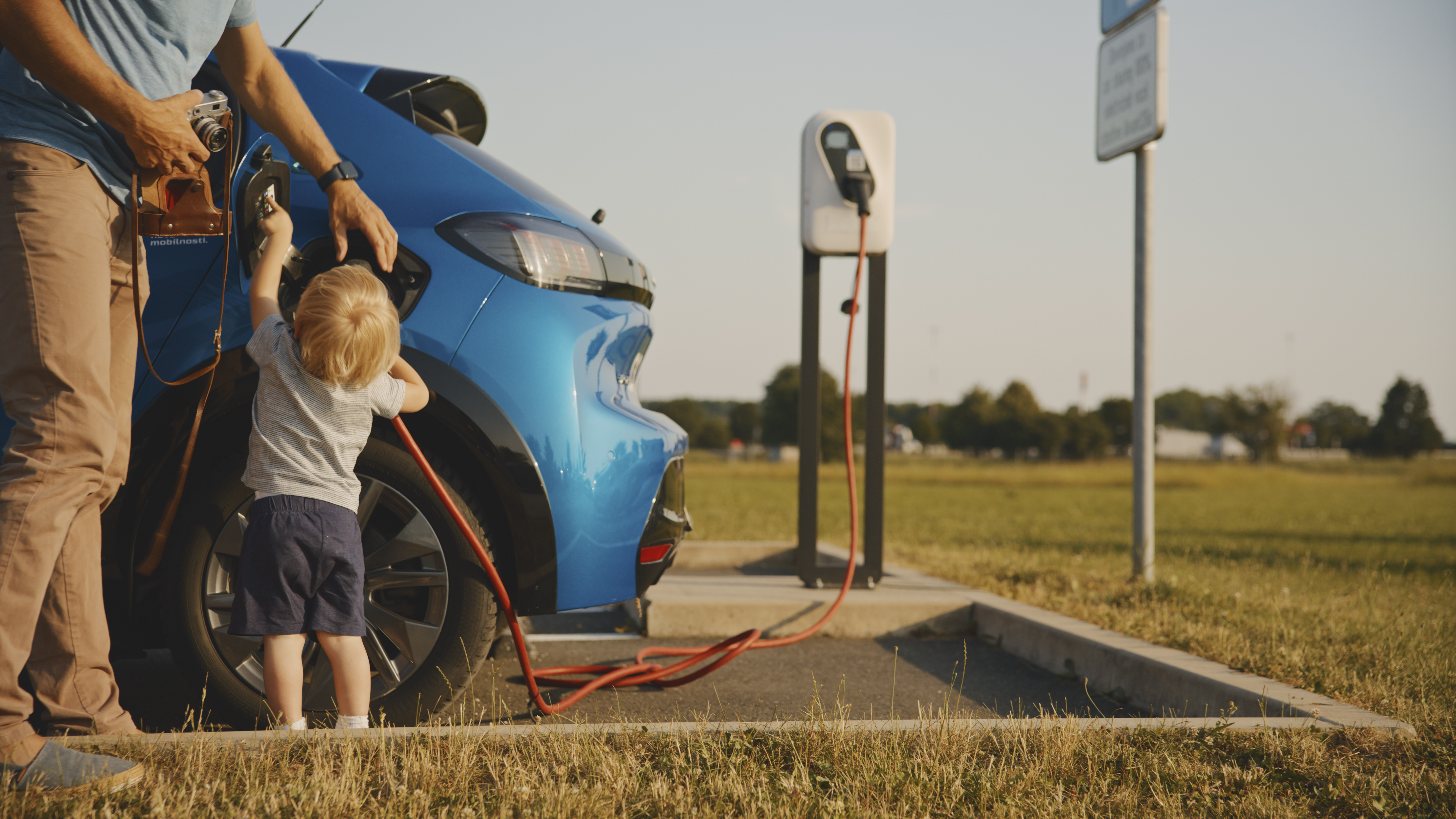 Vater und Kleinkind mit Retrokamera warten auf das Laden des Elektroautos